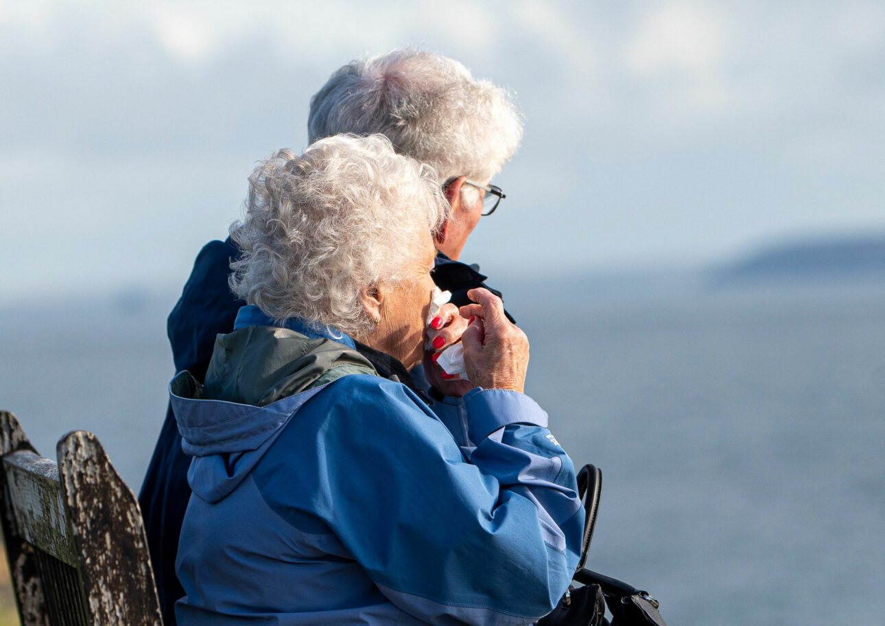 Äldre par som sitter på en bänk vid havet.