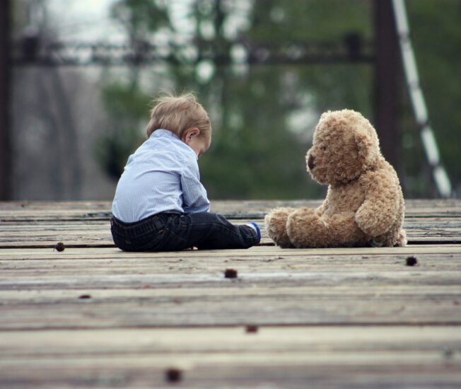 Ett barn som sitter ensamt med en stor teddybjörn