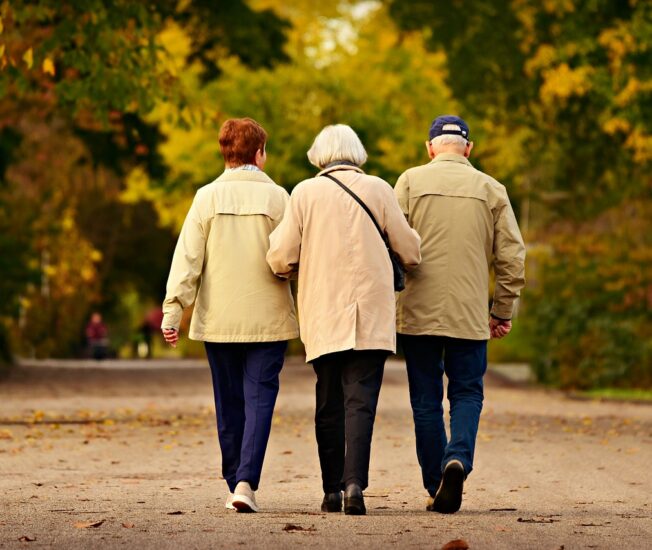 Tre äldre personer promenerar i en park.