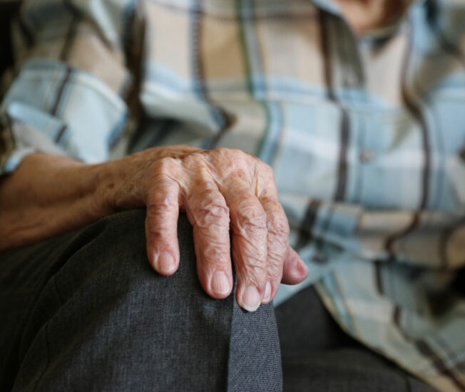 Närbild på äldre person hand som sitter i soffa eller dylikt och håller i en soffkant