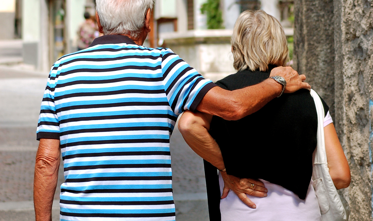 Äldre kvinna och man sedda bakifrån, kvinnan håller sin hand om ryggslutet