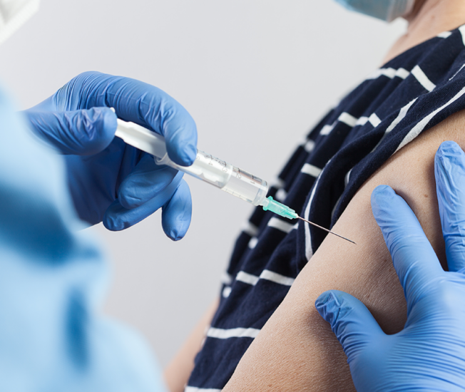 vaccinspruta ges av handskklädd hand till kvinna med upprullad tröjärm