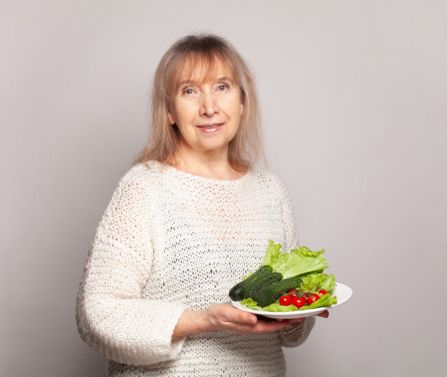Kvinna i övre medelåldern håller i ett fat med färska grönsaker