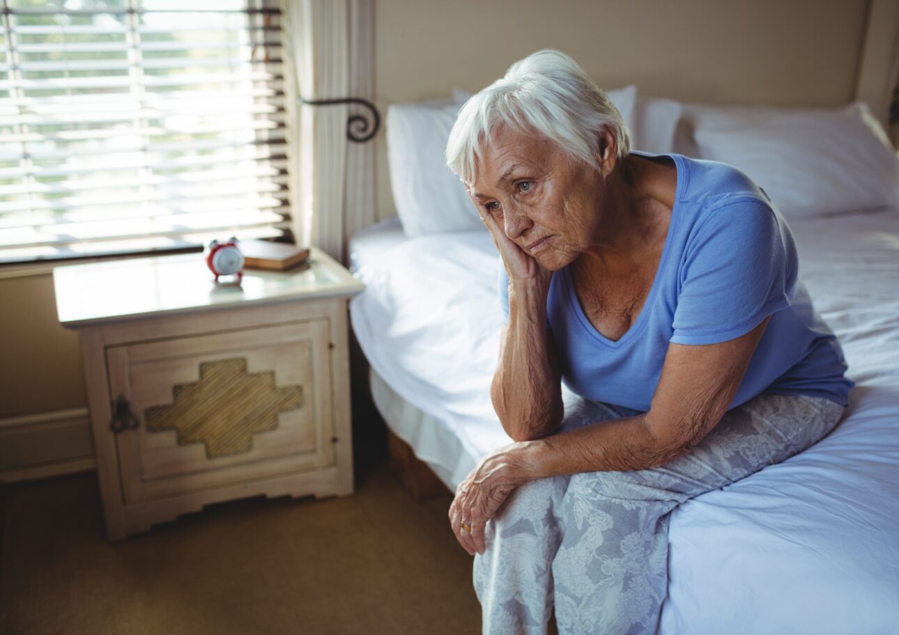 trött äldre kvinna sitter på säng