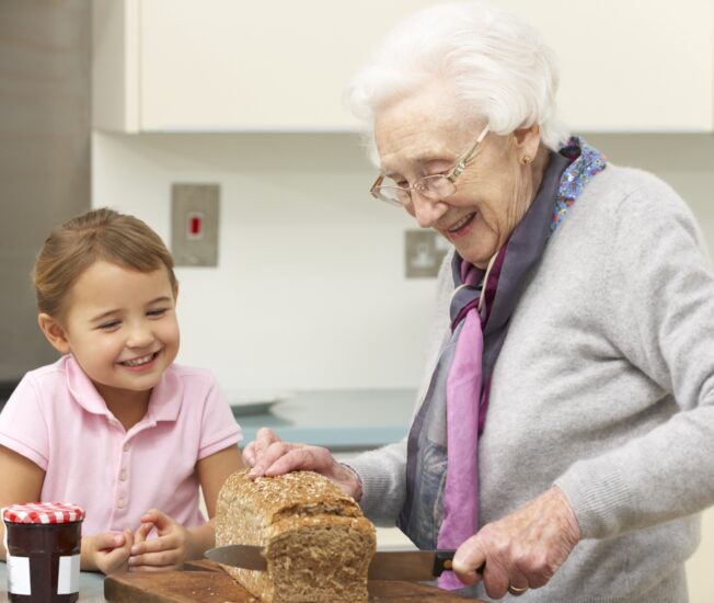 En äldre kvinna och hennes barnbarn fixar mat vid köksbordet.