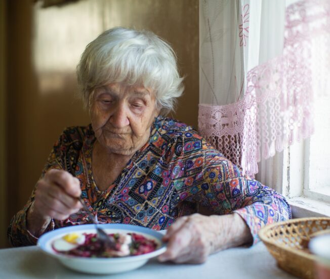 En äldre kvinna sitter vid sitt köksbord och äter