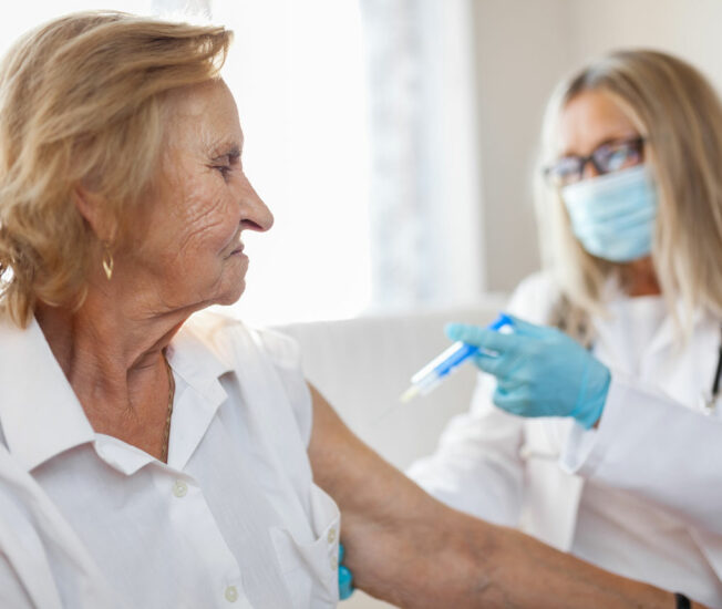 Sköterska ger en äldre kvinna en vaccin via en spruta.