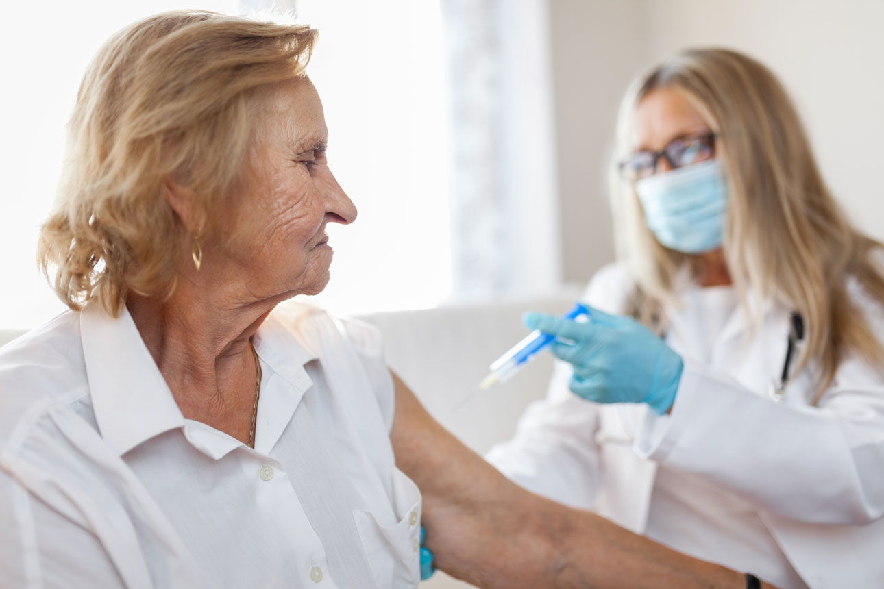Sköterska ger en äldre kvinna en vaccin via en spruta.
