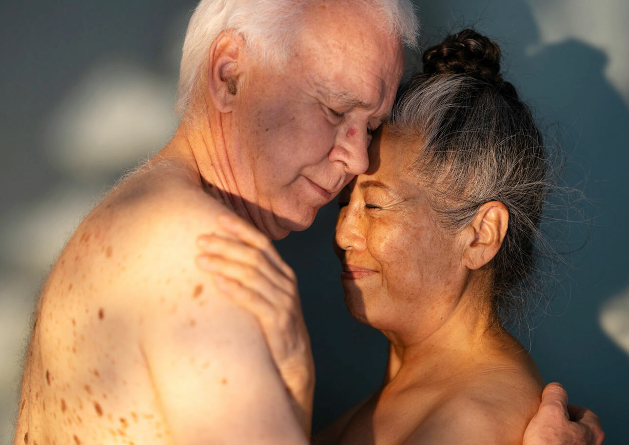 Närbild kvinna och man, båda nakna och 70+, håller ömt om varandra.