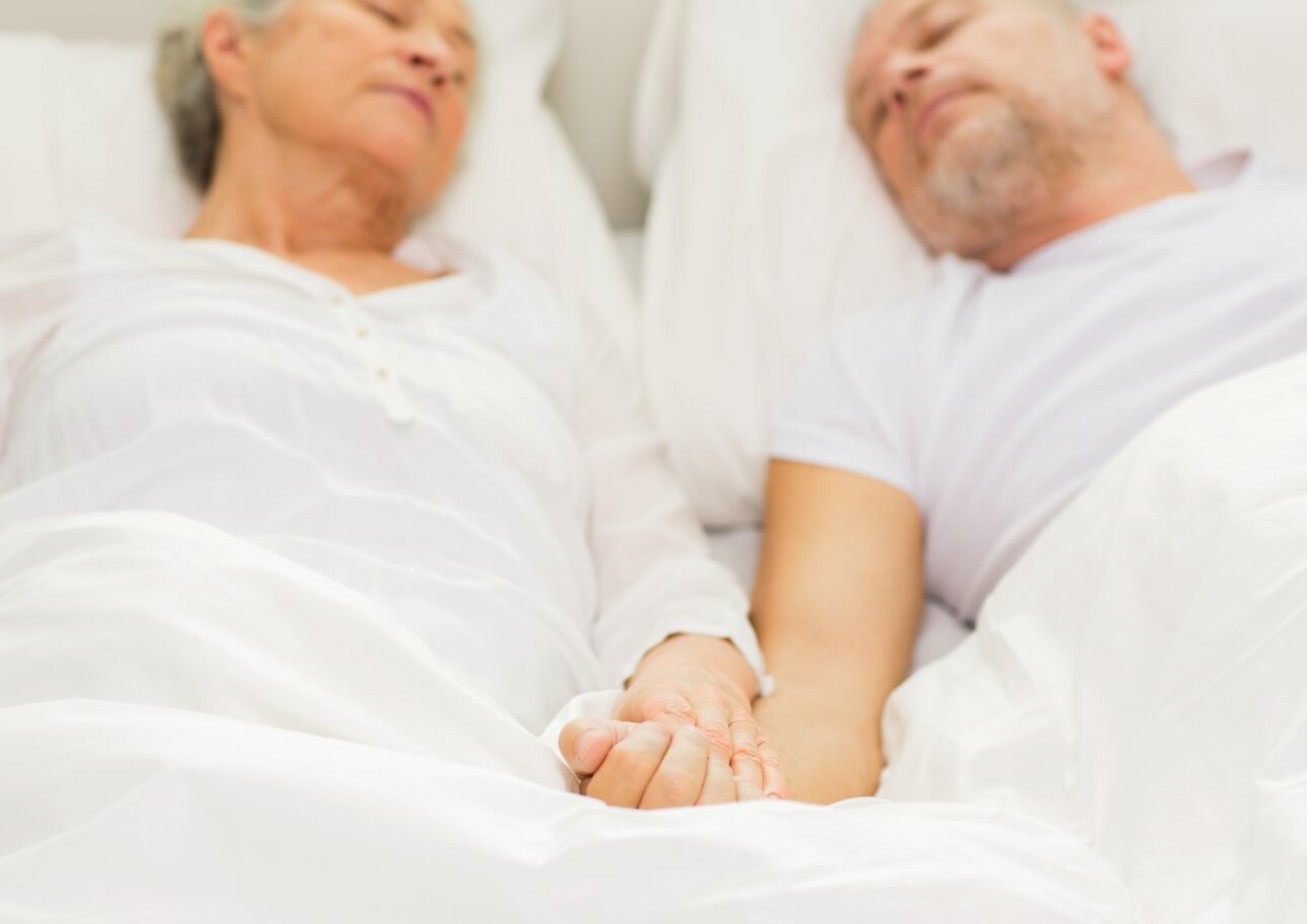 En man och en kvinna ligger i sängen och sover och håller varandra i handen.