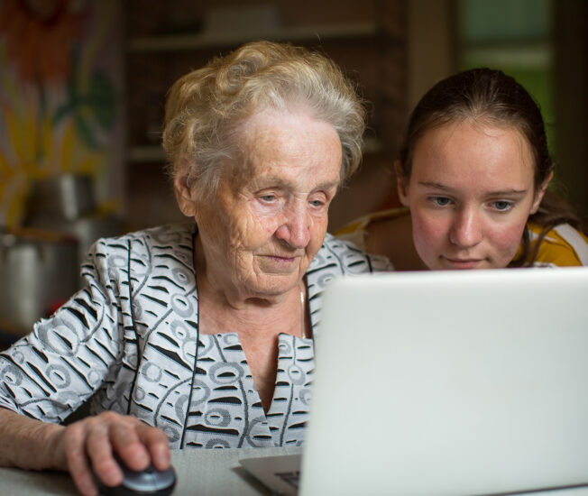 Äldre kvinna och ungdom sitter framför en bärbar dator