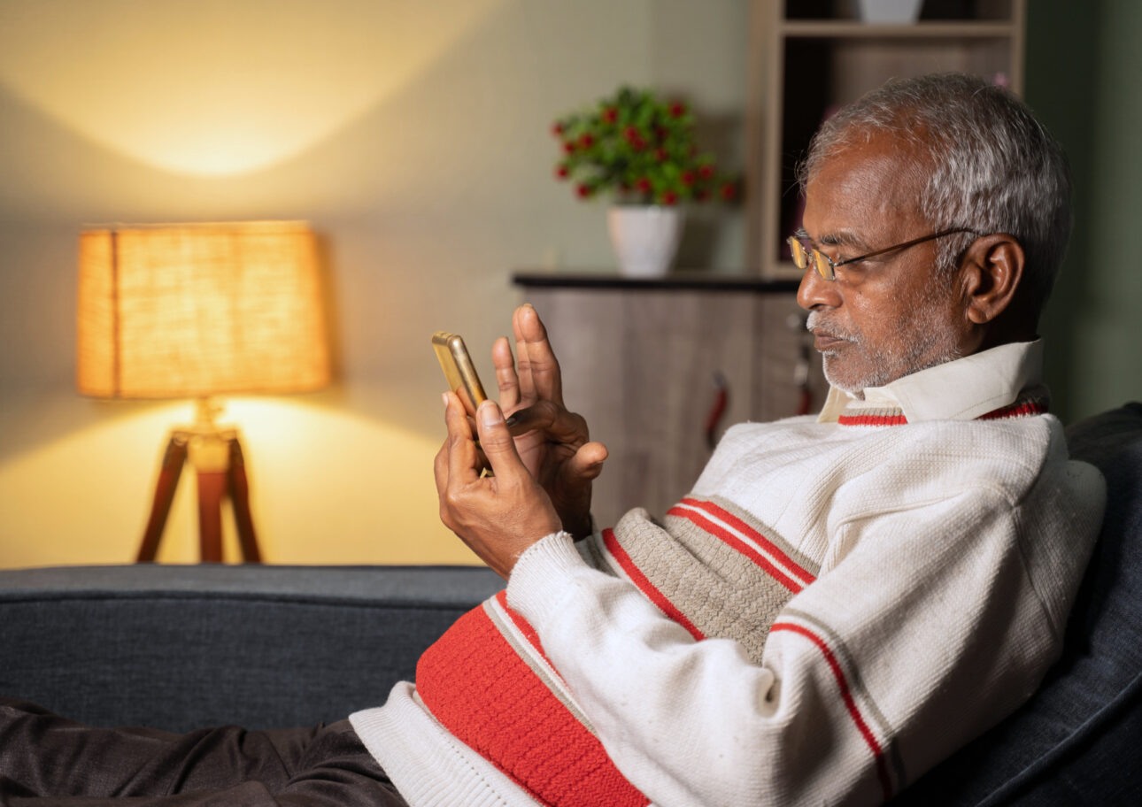 En äldre man sitter i en soffa och tittar på sin mobiltelefon.