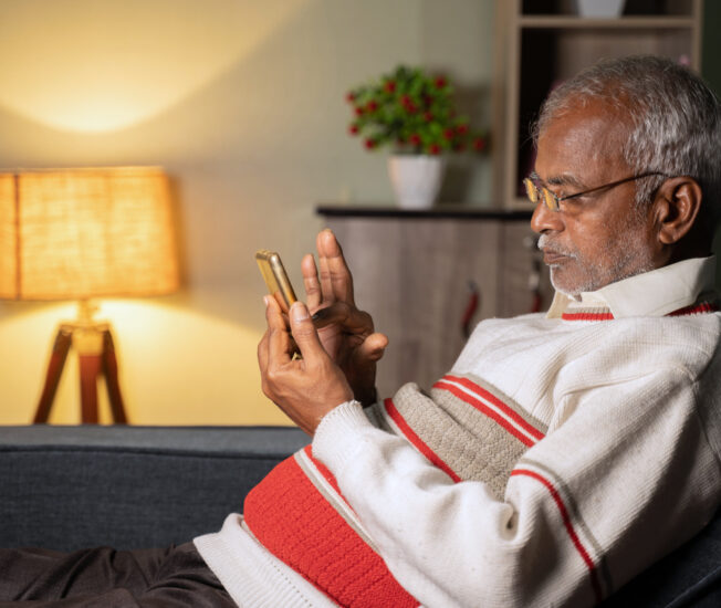 En äldre man sitter i en soffa och tittar på sin mobiltelefon.