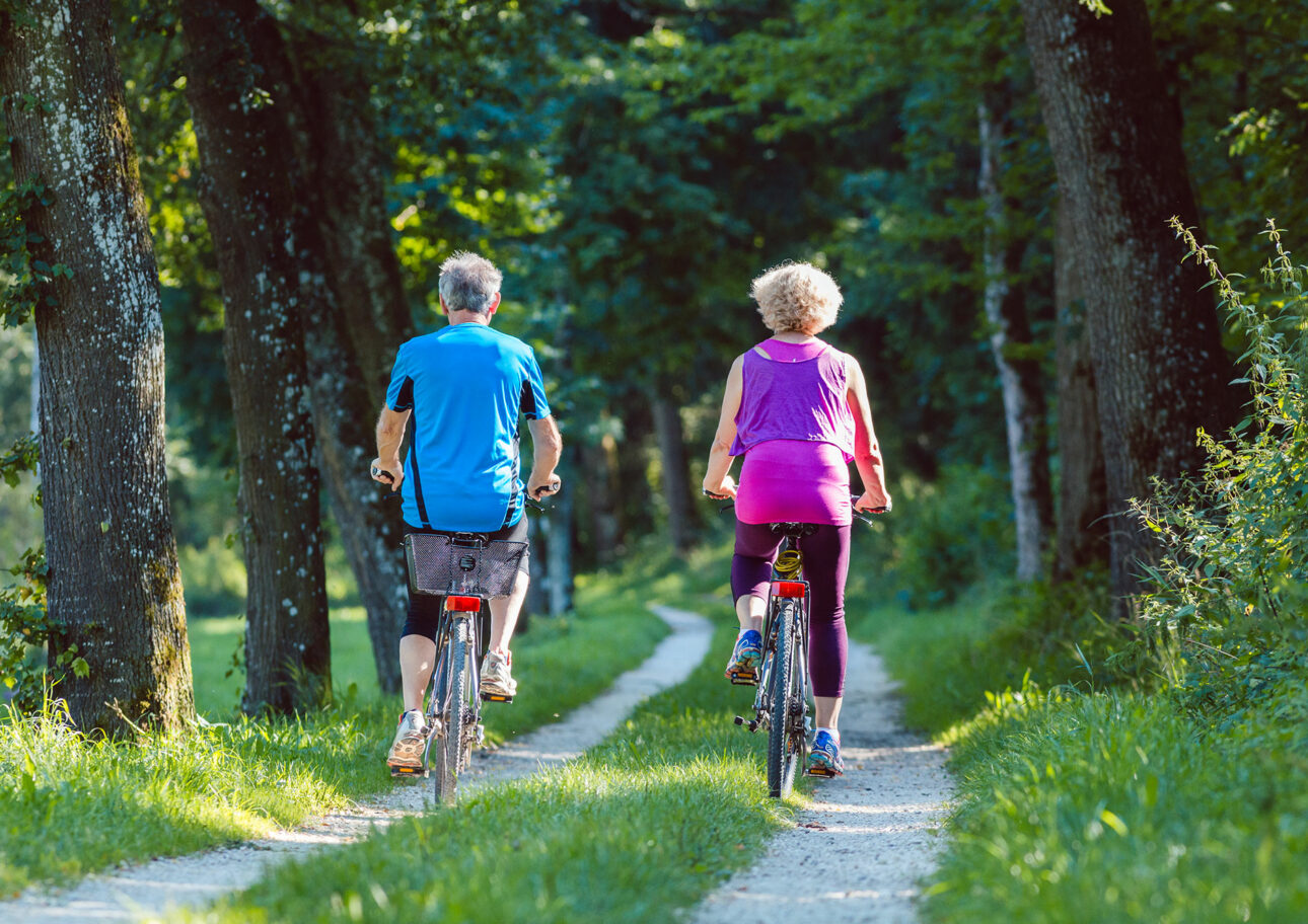 Äldre par cyklar genom skog