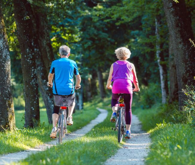 Äldre par cyklar genom skog