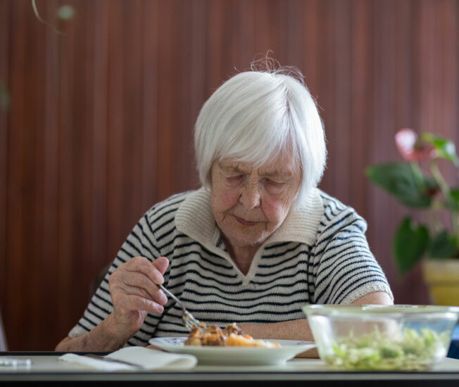 Äldre kvinna sitter och äter mat ensam