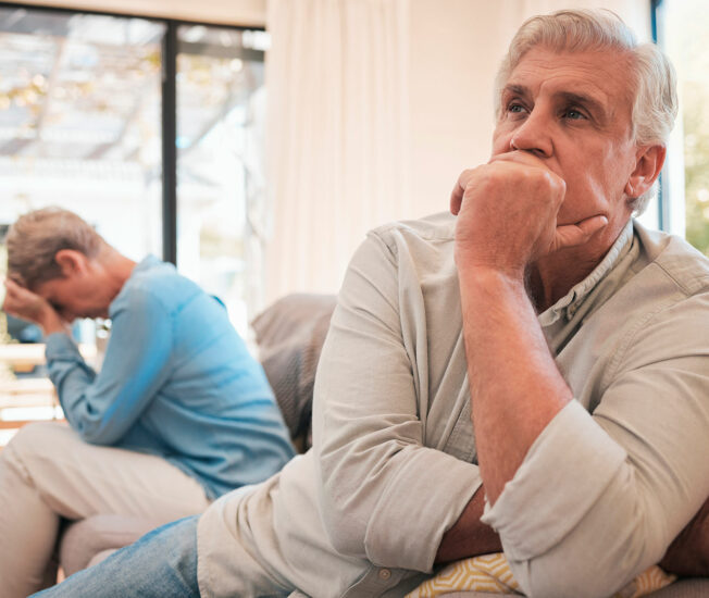 Äldre par sitter i soffa där kvinnan är ledsen, men inte mannen