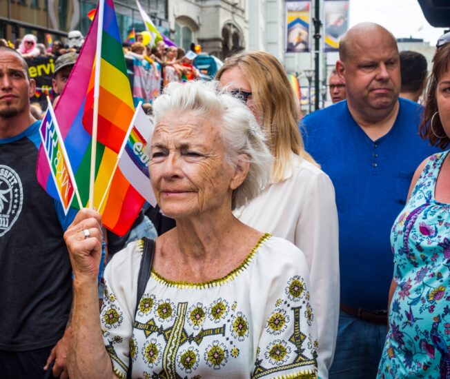 Äldre kvinna vevar prideflagga under parad