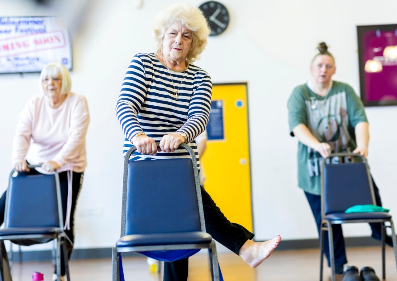 Äldre kvinnor håller i stolar och tränar balansen