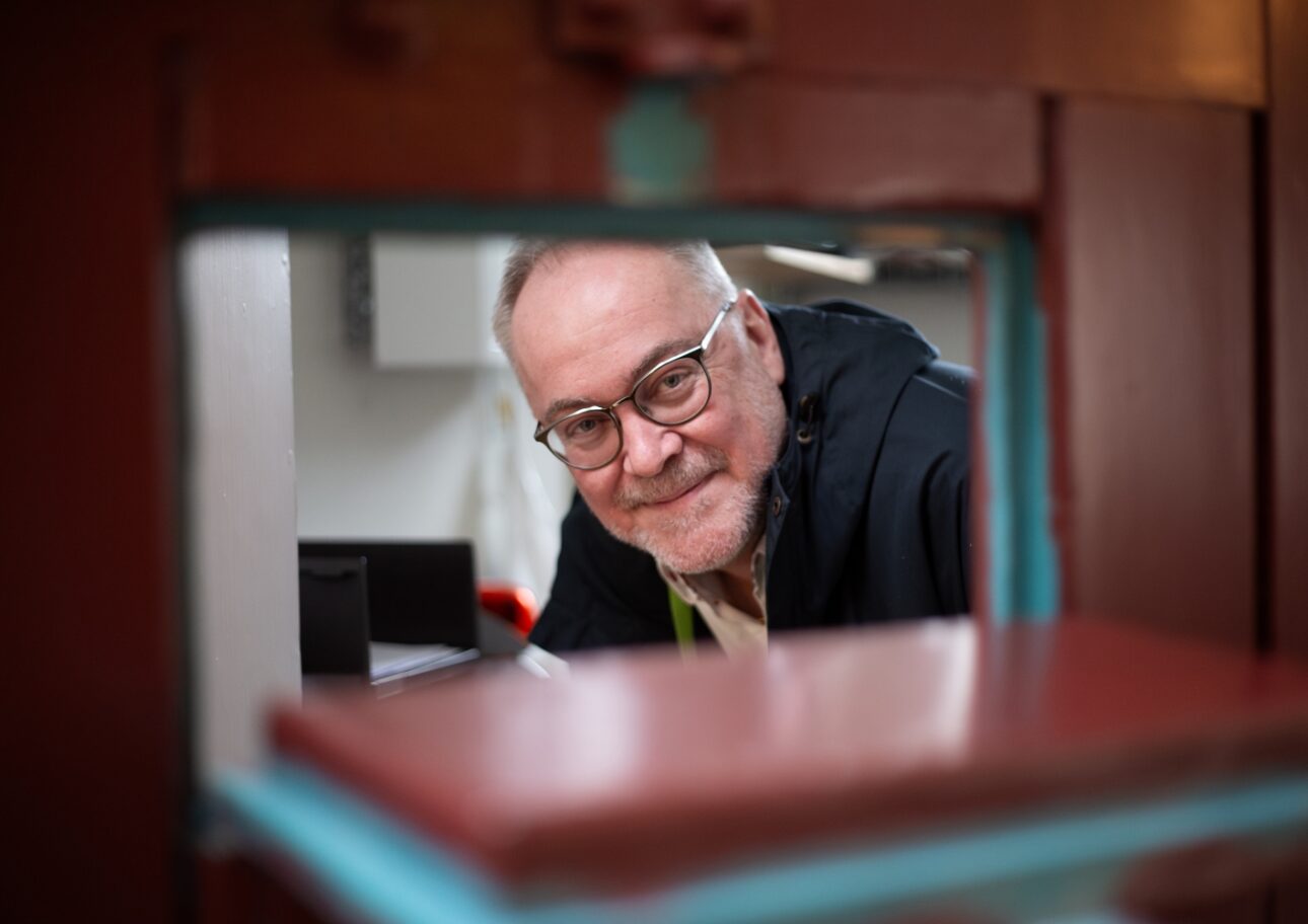 Albert Westergren tittar fram genom en matlucka i en gammal fängelsedörr