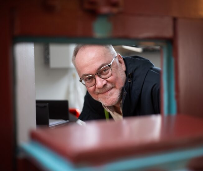 Albert Westergren tittar fram genom en matlucka i en gammal fängelsedörr