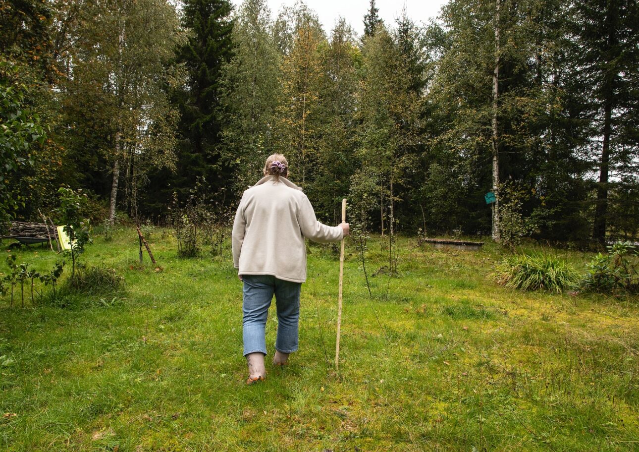 Äldre kvinna går med käpp i skogen