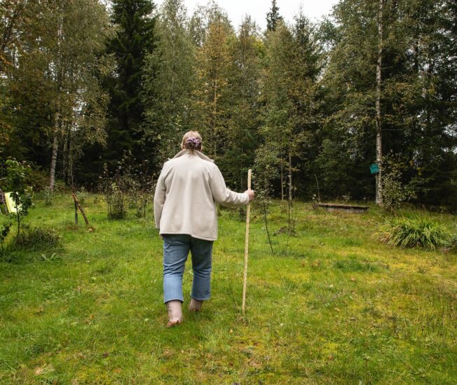Äldre kvinna går med käpp i skogen