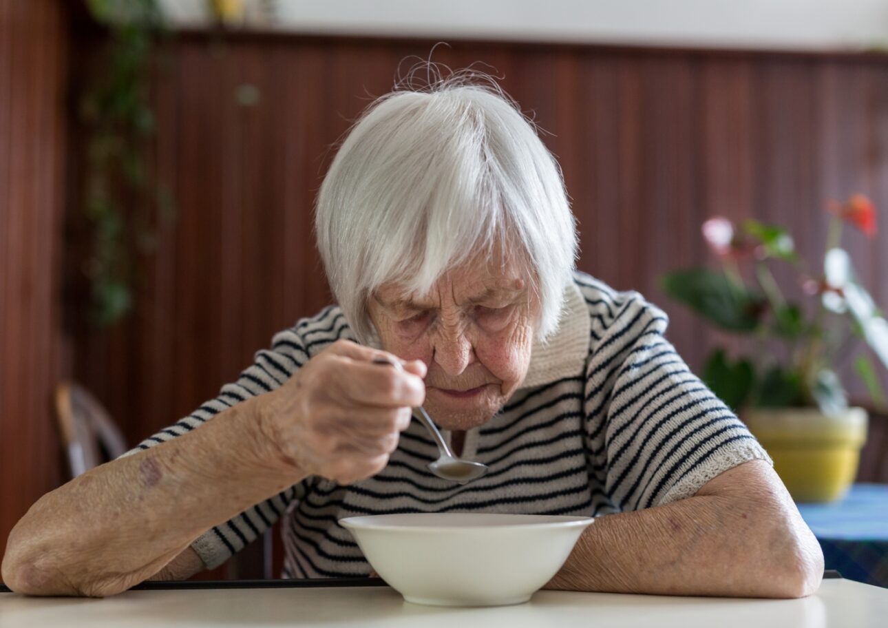Äldre kvinna sitter och äter mat själv