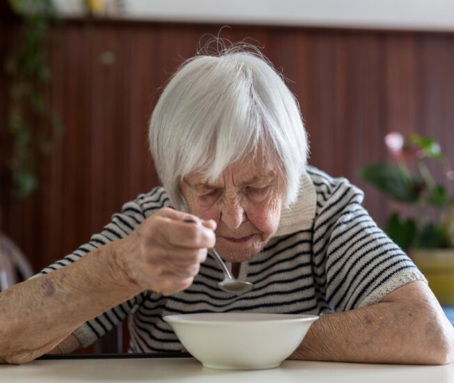 Äldre kvinna sitter och äter mat själv