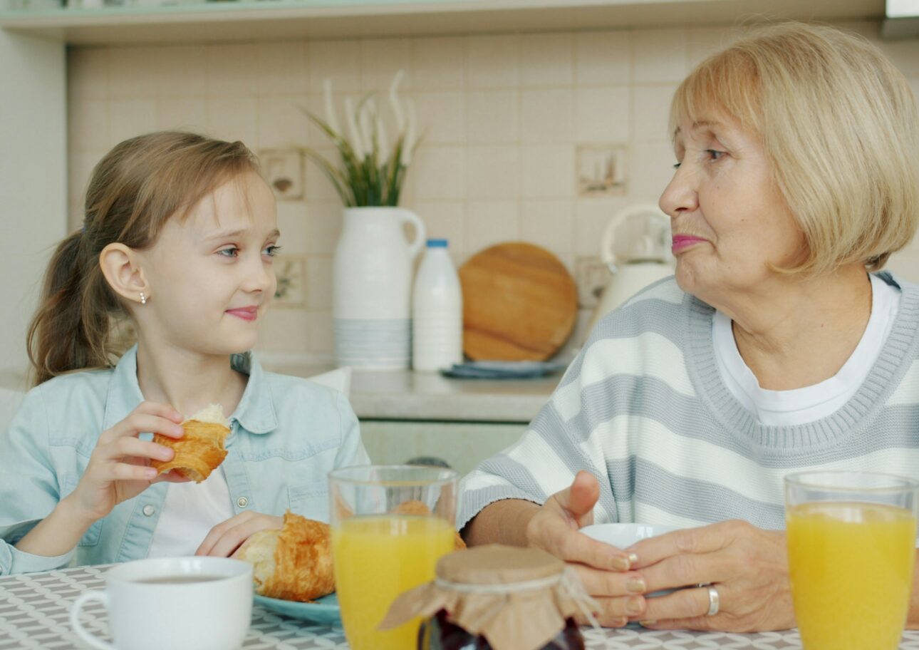 Äldre kvinna sitter vid ett matbord med sitt barnbarn