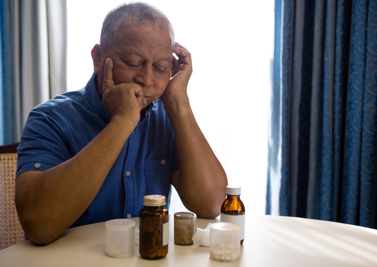 Äldre man tittar på massor av tabletter som ligger på bordet