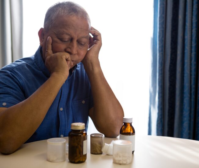 Äldre man tittar på massor av tabletter som ligger på bordet