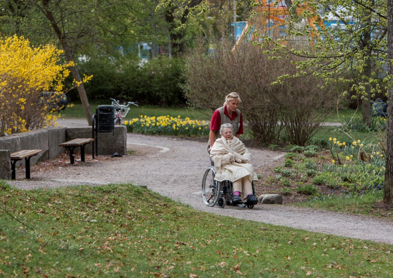Äldre kvinna i rullstol får hjälp med att komma ut