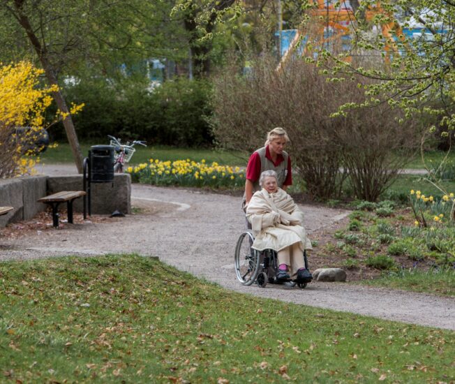 Äldre kvinna i rullstol får hjälp med att komma ut